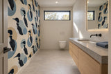 Powder room with a loon-and-circle patterned wall opposite a pale-oak vanity, white tiled basin wall and gray porcelain floor.