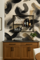 Inky Gesture wallpaper with sweeping black and tan brushstrokes, displayed above a wooden cabinet with glassware.
