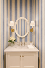 Blue and tan striped wallpaper with a grainstripe pattern, alongside a white oval mirror.
