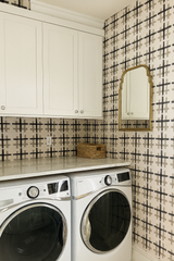 Inkwoven Grid Wallpaper with black and beige cross pattern, visible on a laundry room wall next to cabinets and a mirror.
