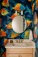 Tropic Chorus wallpaper with fish pattern, on a bathroom wall, accented by a round mirror and light fixtures.
