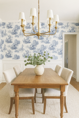 Blue and white toile Harmonie wallpaper with figures and landscapes, complemented by a gold chandelier and wooden dining set.