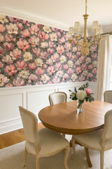 Floral wallpaper with magnolias on a gray background, above white wainscoting, plus a gold chandelier.
