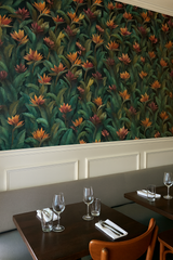 Tropical foliage wallpaper with bird of paradise blooms, covering a dining room wall.