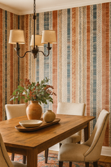 Striped wallpaper with earth-tone patterns, Nomad's Ledger Wallpaper, covering the walls of a dining room with wooden table and chairs.
