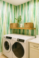 Green Whispering Blades Wallpaper with a painterly pattern, over a laundry room with white appliances and wood shelving.