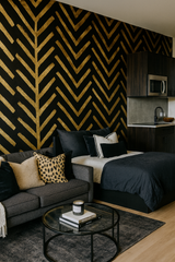 Zulu Gold wallpaper with chevron patterning, in a studio apartment with black and dark wood accents.
