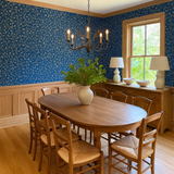 Blue floral Inkwash Brambletrail Wallpaper with vine pattern, covering upper walls above wood paneling in a dining room setting.