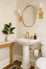 Linen Hatch wallpaper by Schumacher featuring a fine hatched pattern in cream and gold, shown in a bathroom setting.
