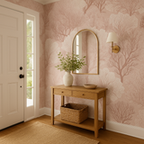 Blush pink wallpaper with coral forest pattern over a white door, table, and mirror.