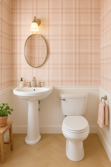 Blush plaid wallpaper with a pattern of intersecting lines, above white wainscoting in a bathroom setting.
