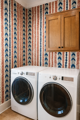 Patterned wallpaper with blue and orange chevron design, Nomad's Chevron Chant Wallpaper, covering laundry room walls.
