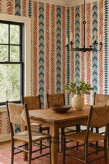 Patterned wallpaper by Nomad's with red and blue chevron motifs covering a beige wall, near a wooden dining set.
