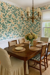 Botanical pattern wallpaper with green leaves by Wildberry Tangle, above the white wainscotting in a dining room setting.
