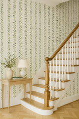 Olive stripe wallpaper with leaf motif, vertical pattern on a wall in an entryway with a staircase.
