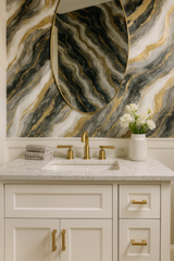 Obsidian Reverie wallpaper with grey, black, and gold marbling, seen behind an oval gold mirror and a white vanity.
