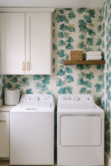 Verdigris Vines Wallpaper with leaf pattern, showing a laundry room with white appliances and light wood shelving.