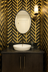 Gold pattern wallpaper with black background, featuring arrow designs and installed around a vanity.
