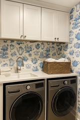 Tea and toile tales wallpaper with blue teapots and flowers, covering the wall behind a sink and laundry machines.