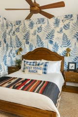 Botanical blueprint wallpaper with blue leaf pattern on an off-white background covering the walls in a bedroom.