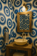 Floral wallpaper with sunburst pattern, textured with blue and white, reflected in a wooden-framed mirror.