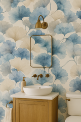 Mistleaf Whisper wallpaper with blue and tan ginkgo leaf pattern, covering a bathroom wall with vanity and fixtures.
