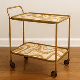 Gold two-tier bar cart featuring mocha mirage patterned trays, against a neutral wall.