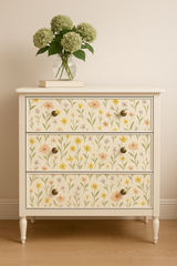 Wildflower Waltz wallpaper with a dainty floral pattern, covering a cream-colored chest of drawers with brass knobs.