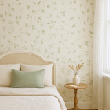 Green botanical wallpaper with climbing ivy pattern, on a bedroom wall behind a bed and bedside table.
