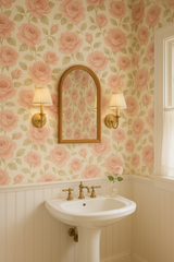 Floral wallpaper by York Wallcoverings with a pink rose pattern on a cream background, visible behind a white pedestal sink and wooden-framed mirror.
