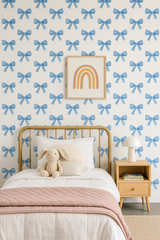 Bluebell Bows Wallpaper with a blue bow pattern, decorating a child's bedroom with a bed, nightstand and art.
