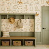 Prairie Rider Wallpaper with cowboy-themed pattern on a beige wall behind a sage green mudroom storage bench.
