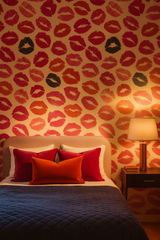 Patterned wallpaper with red kisses by unknown designer, covering a bedroom wall with a lamp and furniture.
