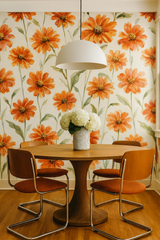 Sun-Kissed Tithonia Wallpaper featuring an orange floral pattern, covering a wall above a round wooden table with chairs.
