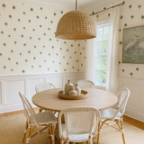 Palm tree patterned wallpaper with white wainscoting, complemented by a round wooden dining table and rattan light fixture.
