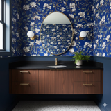 Floral wallpaper with magnolia pattern on blue background, with vanity and oval mirror.