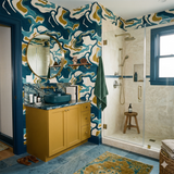 Colorful patterned wallpaper with shades of blue and gold, with a marbled vanity and brass fixtures.
