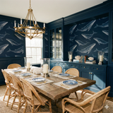 Pelagic Lineage wallpaper with whale pattern, on a navy blue wall behind a dining table.
