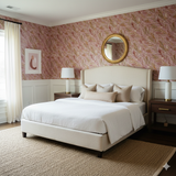 Patterned Rosette Vale wallpaper with pink and gold accents, decorating a bedroom wall with framed art and a round mirror.