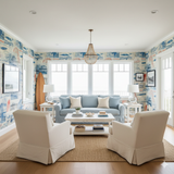 Shoreline Souvenir wallpaper with souvenir themed patterns, decorating a living room with a blue couch and white armchairs.