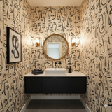 Atelier Faces Wallpaper with sketched face pattern, covering bathroom walls around a gold-rimmed mirror.
