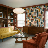Patterned wallpaper with earth tones and geometric shapes near mid-century modern furniture.