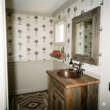 Stockyard No. 17 Wallpaper with windmill pattern, over wainscoting in a rustic bathroom.