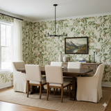 Buckeye Grove wallpaper with green leaf pattern, covering a dining room wall, with a dark wood table and beige upholstered chairs.