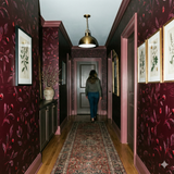 Deep red botanical wallpaper featuring leaves and berries, set in a hallway with a central rug.
