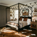 Redrock Signal Wallpaper with a repeating animal skull pattern, applied in a bedroom with cowboy art and a brown hide rug.