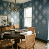 Slate blue floral wallpaper with a botanical pattern on the wall behind a round dining table.