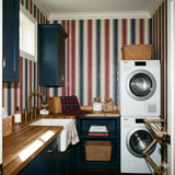 Striped wallpaper in red, white, and blue regatta pattern against blue cabinets and a stacked washer and dryer.