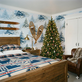 Frostpine Valley Wallpaper with a snowy forest scene, styled in a cozy, rustic bedroom with warm wood tones.
