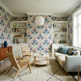 Floral Folk & Fire Wallpaper with a blue and red pattern covering the walls of an interior with bookshelves.
